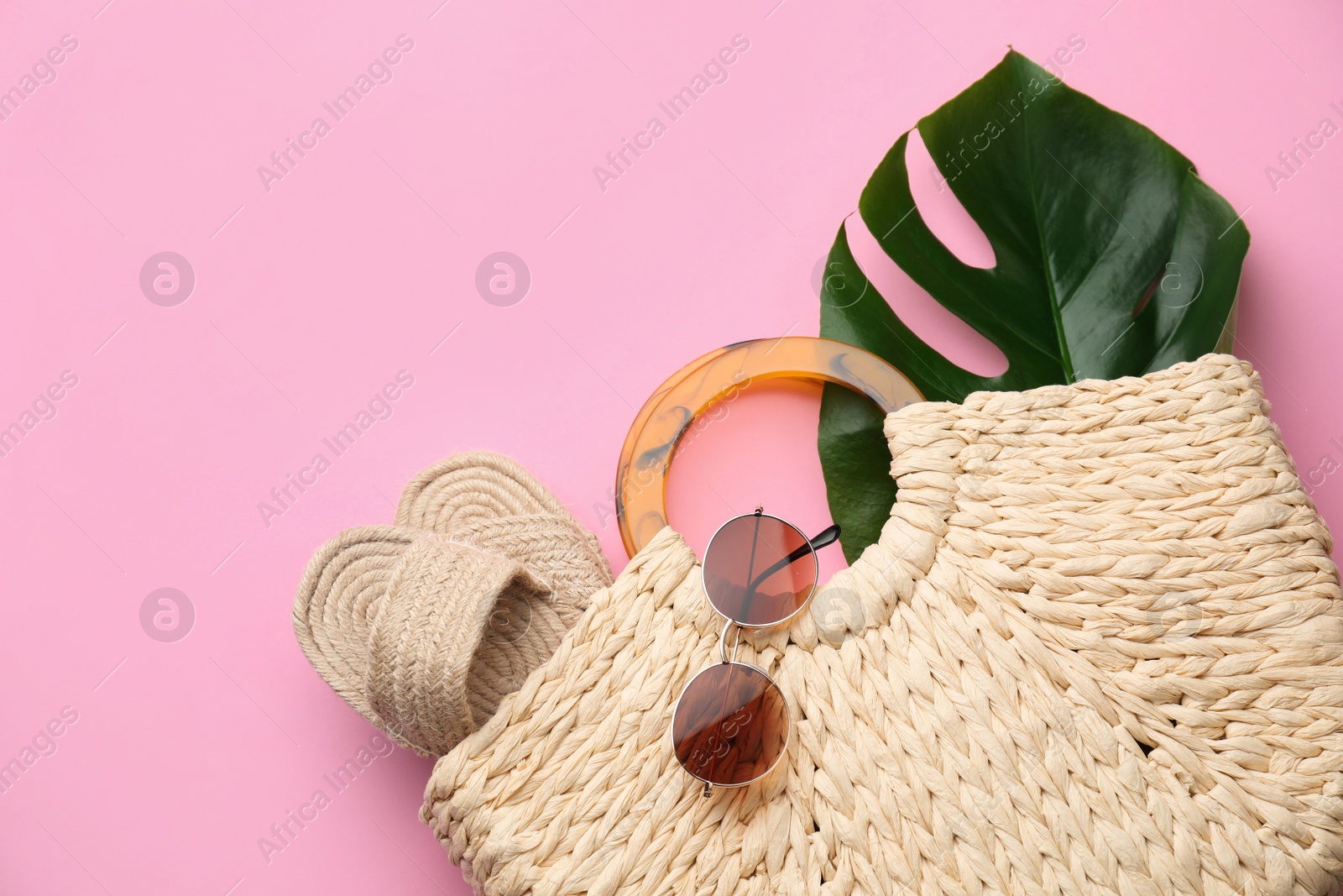 Photo of Elegant woman's straw bag with shoes, tropical leaf and sunglasses on pink background, top view
