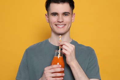Handsome young man with glass of juice on orange background