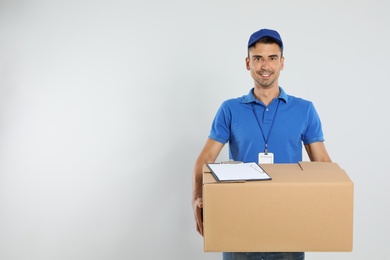Photo of Happy young courier with cardboard box and clipboard on white background. Space for text
