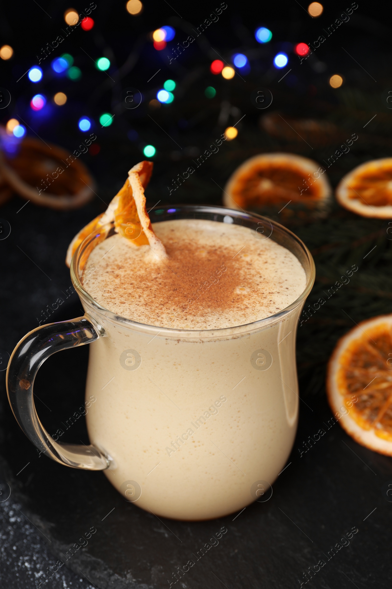 Photo of Glass cup of delicious eggnog with dried orange slice and cinnamon on black table