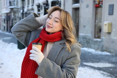 Photo of Portrait of charming woman with paper cup of coffee on city street in winter