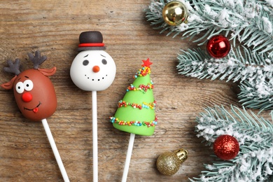 Photo of Delicious Christmas themed cake pops and fir tree branches with balls on wooden table, flat lay
