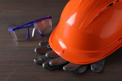 Photo of Hard hat, goggles and gloves on wooden table, closeup. Safety equipment