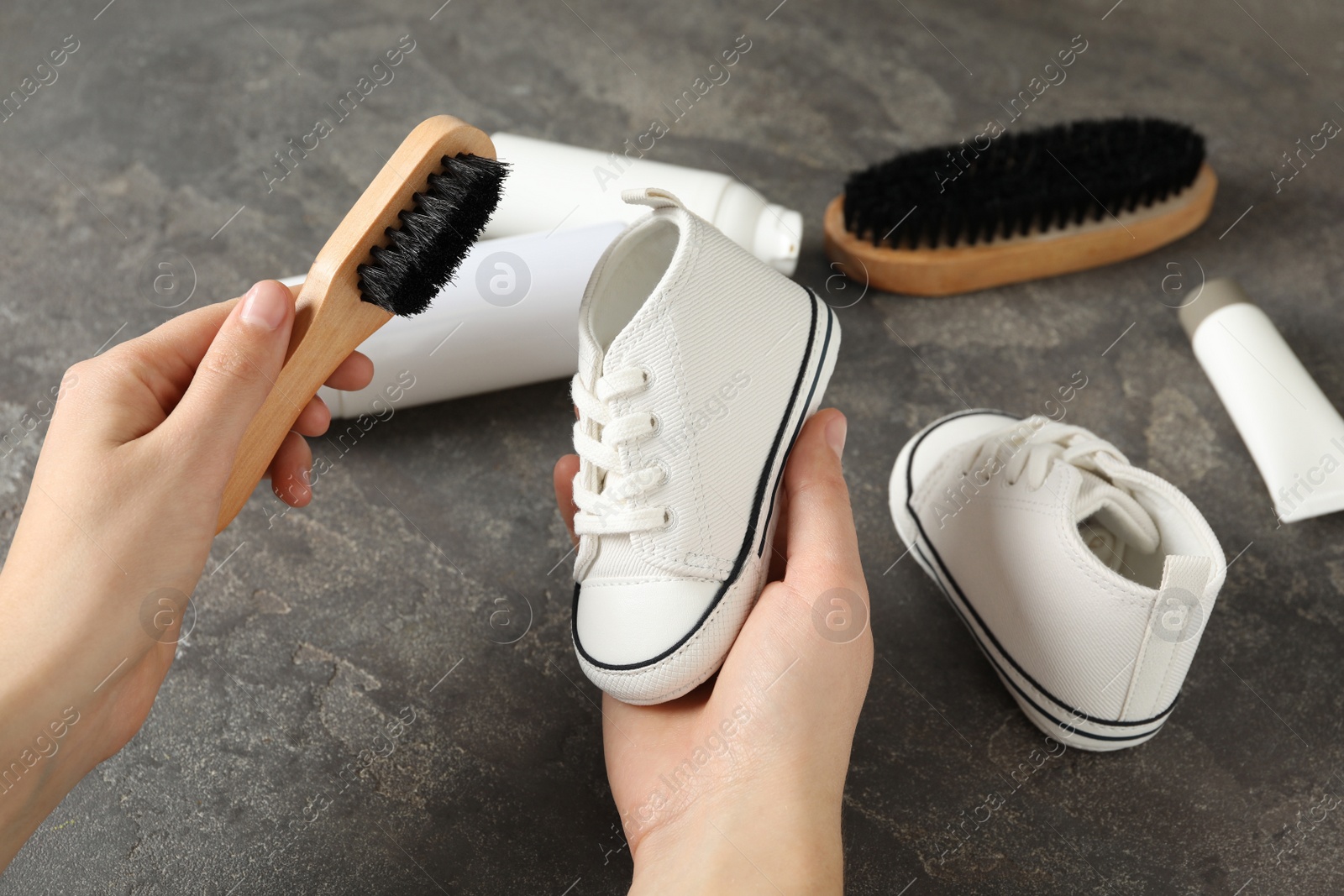 Photo of Woman cleaning stylish footwear on grey stone background, closeup. Shoe care accessories