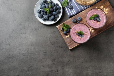 Photo of Glasses of tasty blueberry smoothie with oatmeal on dark grey table, flat lay. Space for text