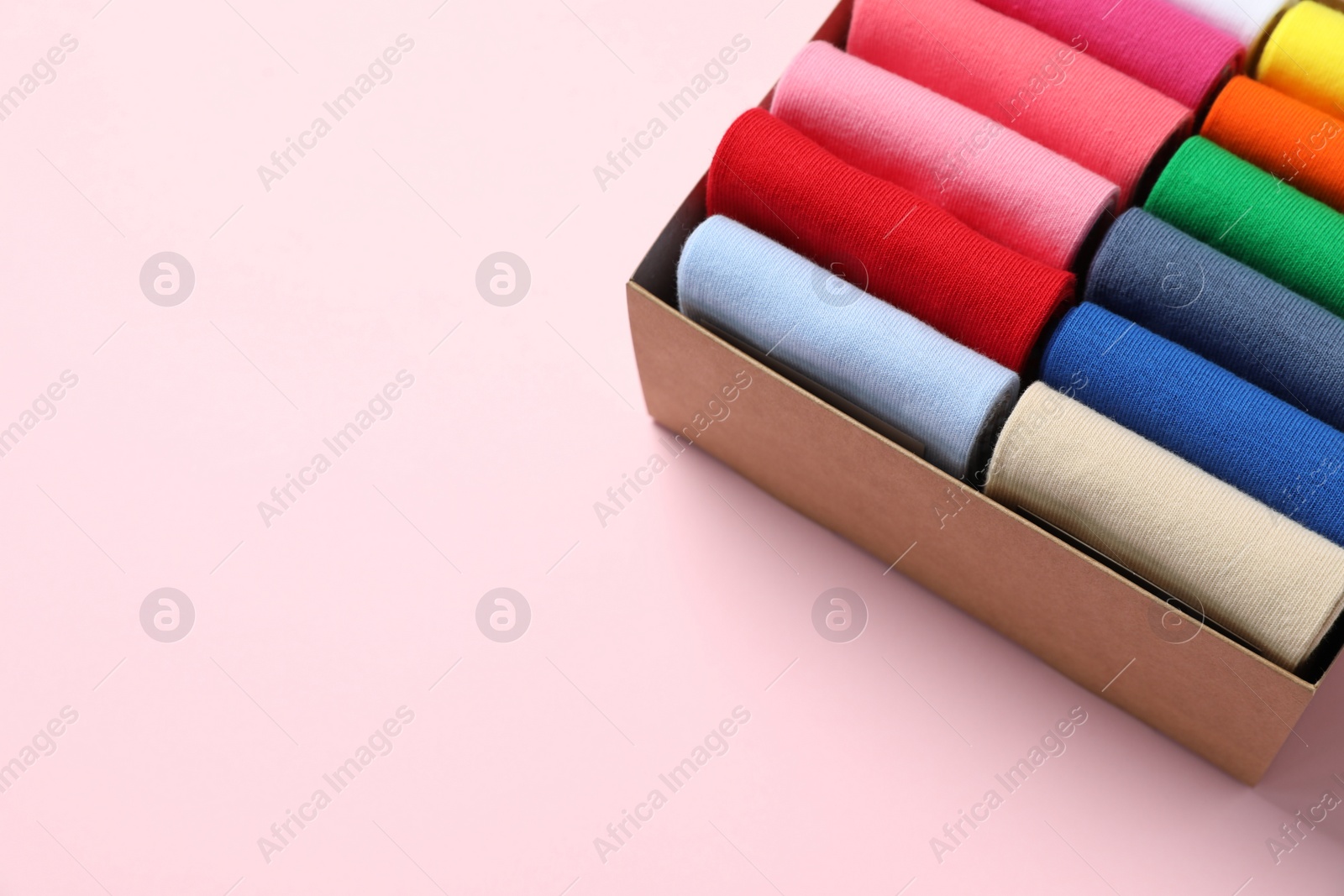 Photo of Box with different colorful socks on light pink background. Space for text