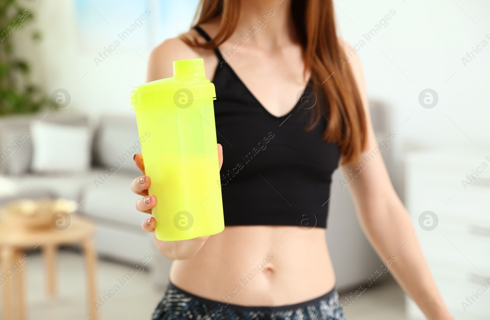 Photo of Young woman with bottle of protein shake at home, closeup view
