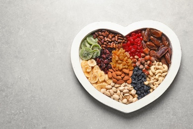 Photo of Heart shaped plate with different dried fruits and nuts on table. Space for text