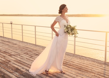 Photo of Gorgeous bride in beautiful wedding dress with bouquet near river on sunset