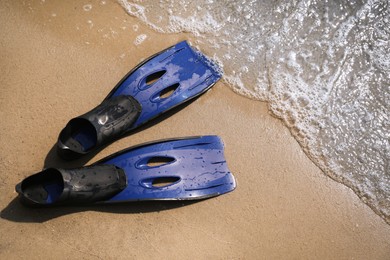 Pair of blue flippers on sand near sea, top view
