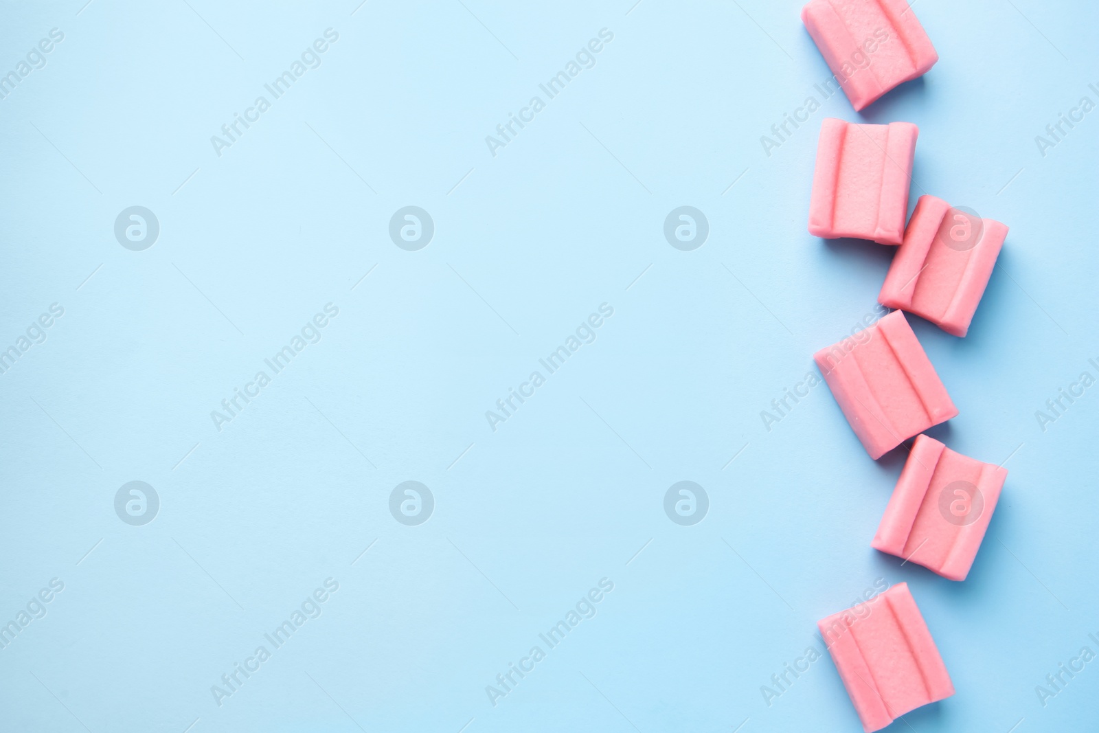 Photo of Tasty chewing gums on light blue background, flat lay. Space for text