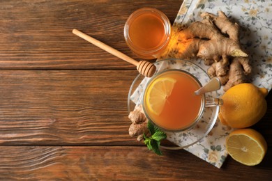 Photo of Cupdelicious ginger tea, honey and lemons on wooden table, flat lay. Space for text