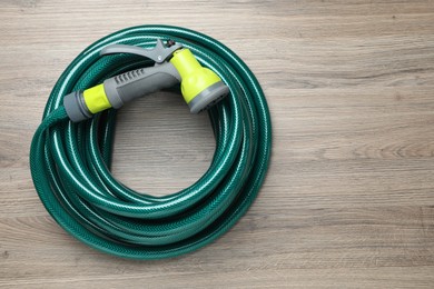 Photo of Green rubber watering hose with nozzle on wooden surface, top view