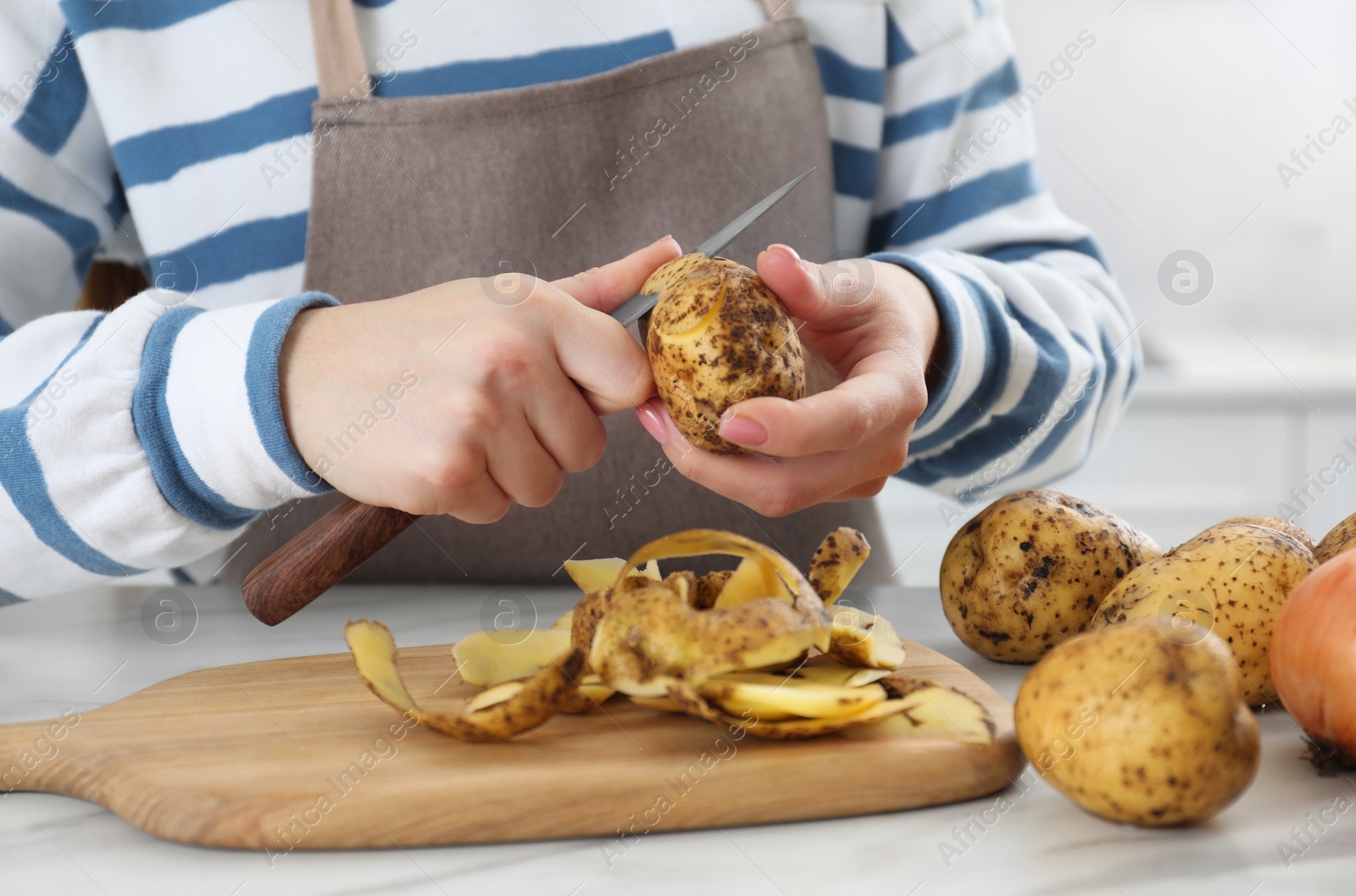 Photo of Woman peeling fresh potato with knife at white marble table indoors, closeup