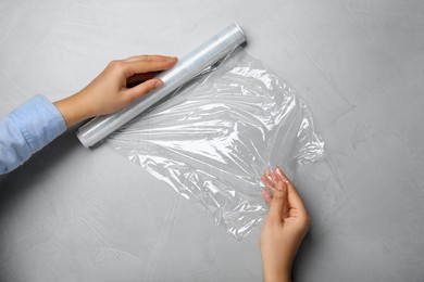 Photo of Woman with roll of stretch wrap at light grey table, top view