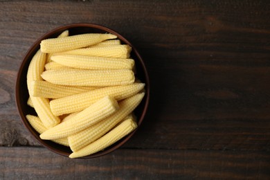 Photo of Tasty fresh yellow baby corns in bowl on wooden table, top view. Space for text