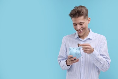 Photo of Happy man putting coins into piggy bank on light blue background. Space for text