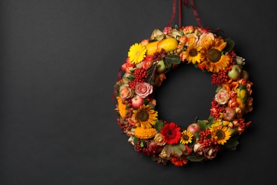 Photo of Beautiful autumnal wreath with flowers, berries and fruits hanging on black background. Space for text