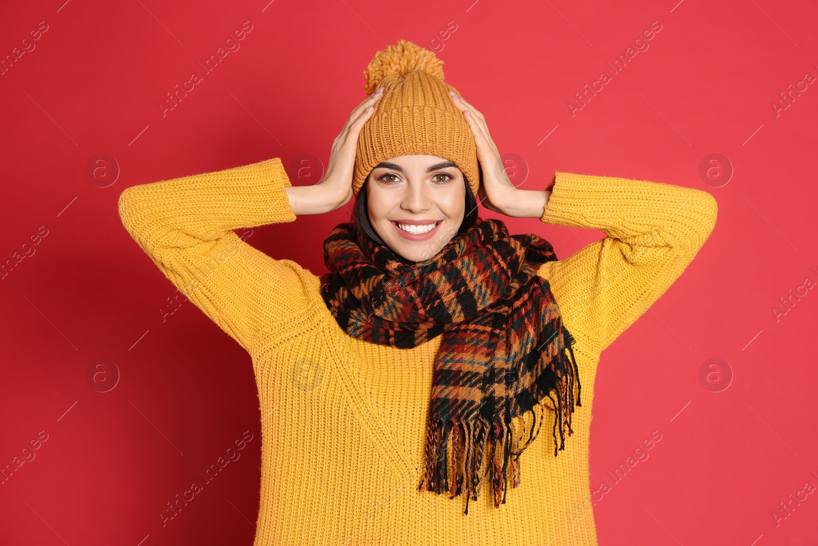 Photo of Young woman wearing warm sweater, scarf and hat on red background. Winter season