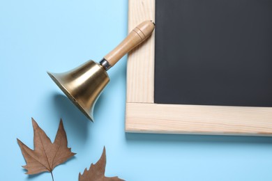 Golden school bell, autumn leaves and blackboard on light blue background, flat lay