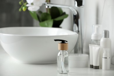 Photo of Bottle with dispenser cap and cosmetic products on white table in bathroom