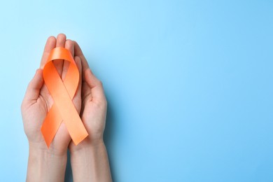 Photo of Man holding orange ribbon on light blue background, top view with space for text. Multiple sclerosis awareness
