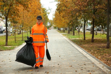 Photo of Street cleaner with broom and garbage bag outdoors on autumn day