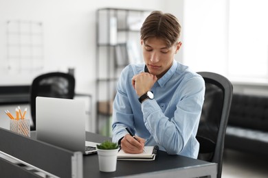 Photo of Man taking notes during webinar at table in office