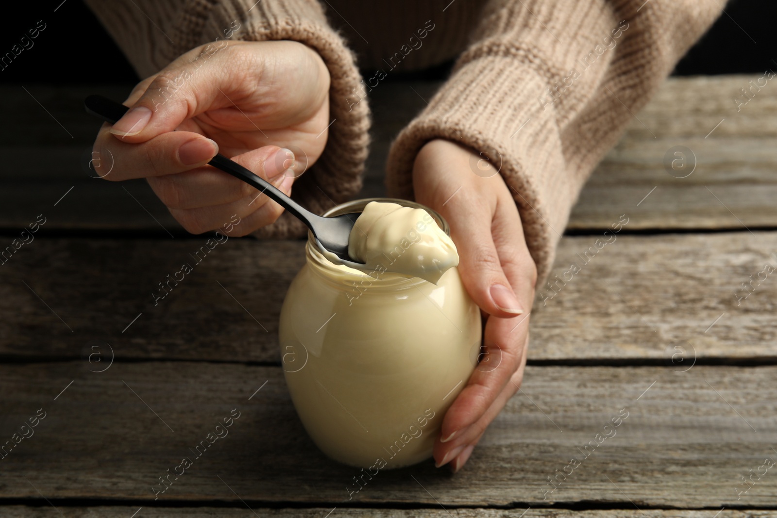 Photo of Woman with jar of delicious mayonnaise at wooden table, closeup