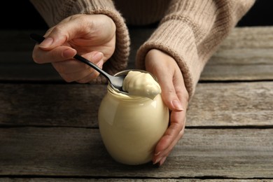 Photo of Woman with jar of delicious mayonnaise at wooden table, closeup