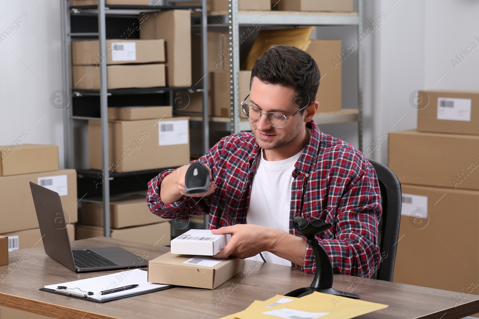 Photo of Seller with scanner reading parcel barcode at table in office. Online store