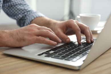 Man working with modern laptop at wooden table indoors, closeup