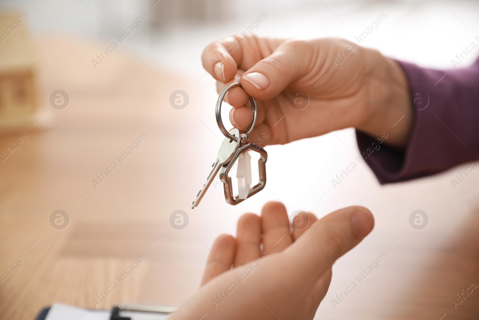 Photo of Real estate agent giving key with trinket to client in office, closeup