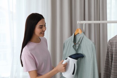 Photo of Woman steaming shirt on hanger at home