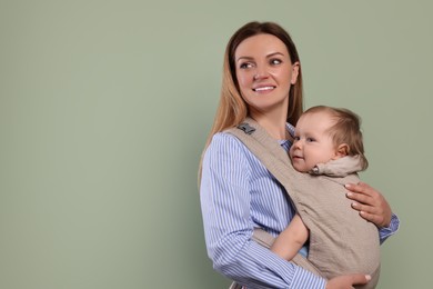 Mother holding her child in sling (baby carrier) on olive background. Space for text