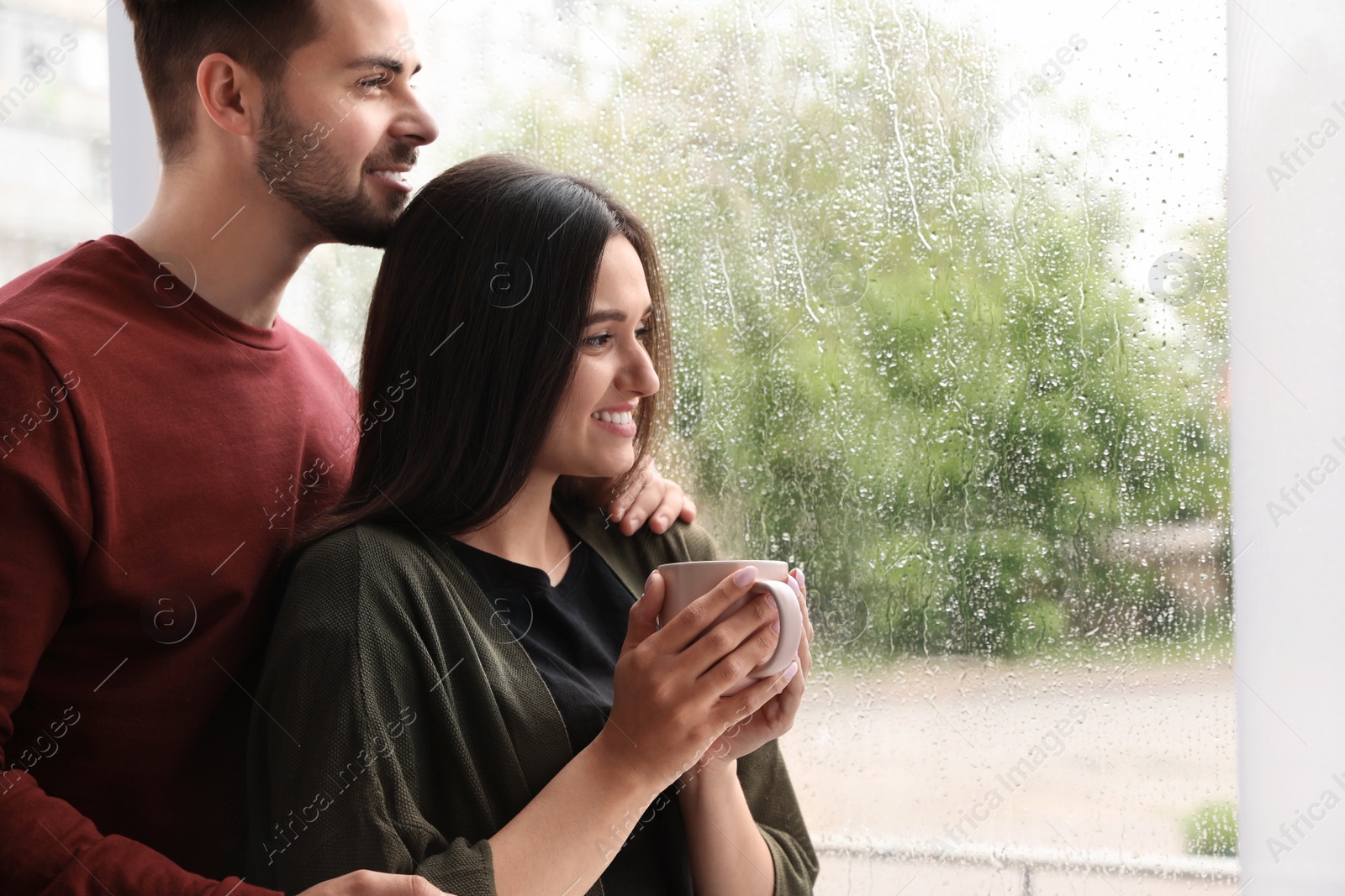 Photo of Happy young couple near window indoors on rainy day