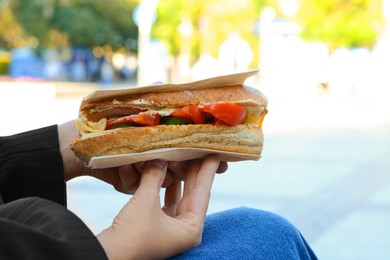 Photo of Woman holding tasty sandwich with vegetables outdoors, closeup. Street food