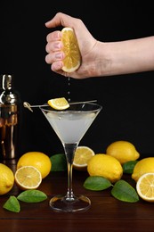Woman squeezing lemon into Martini cocktail at wooden table, closeup