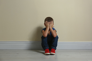 Little boy closing face with hands on floor near yellow wall. Child in danger