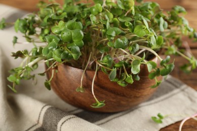 Fresh radish microgreens in bowl on wooden table, closeup