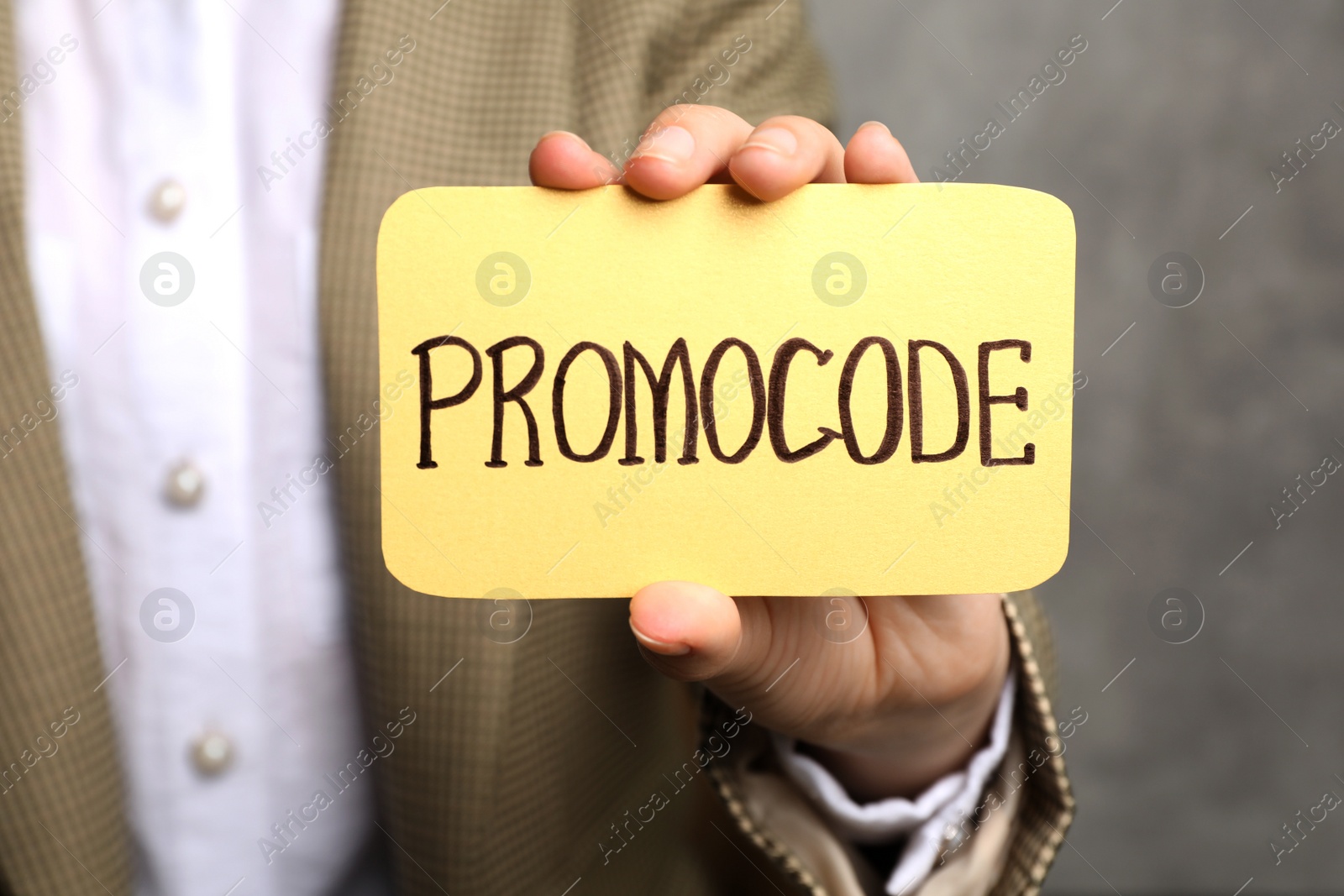 Photo of Woman holding card with words Promo Code on grey background, closeup