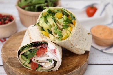 Delicious sandwich wraps with fresh vegetables and sauce on white wooden table, closeup