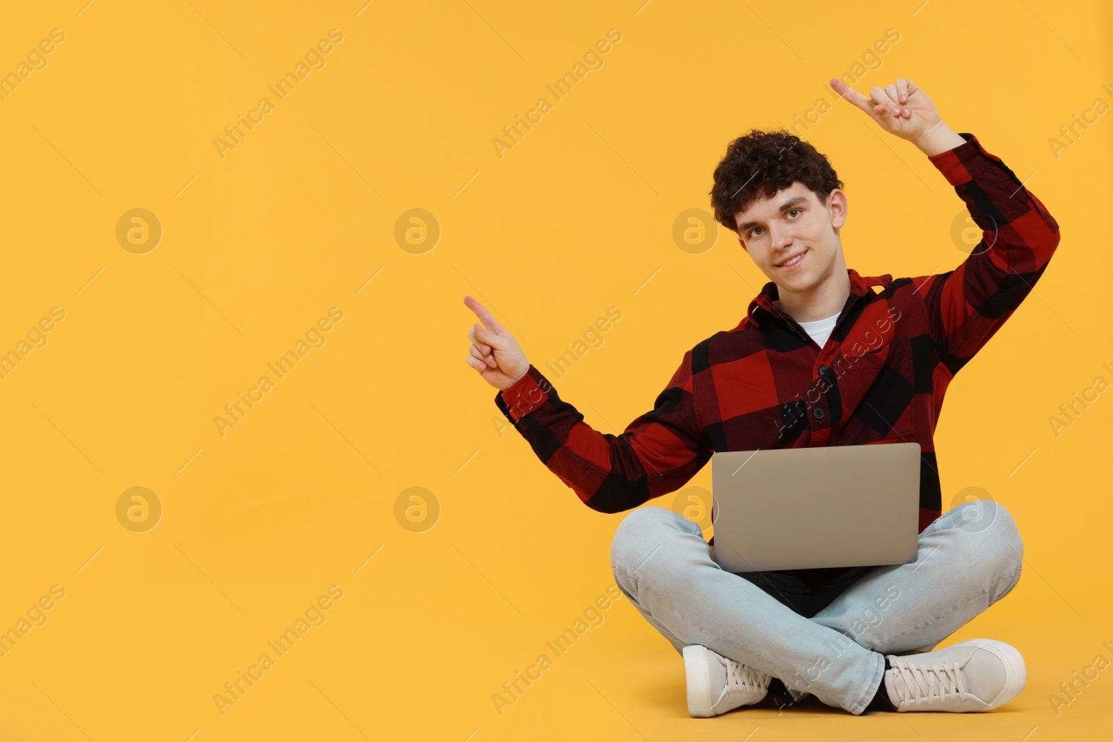 Photo of Portrait of student with laptop pointing on orange background. Space for text