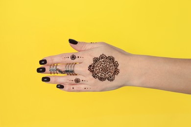 Photo of Woman with henna tattoo on hand against yellow background, closeup. Traditional mehndi ornament