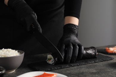 Chef in gloves cutting sushi roll at dark textured table, closeup