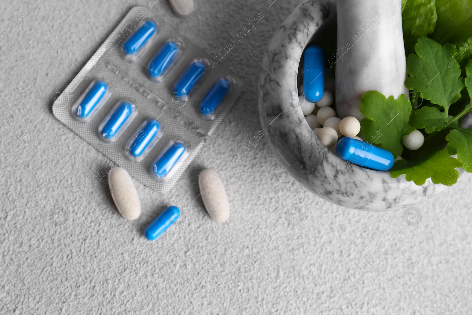 Photo of Marble mortar with fresh green herbs and pills on white table, flat lay