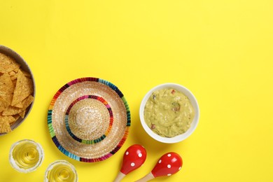 Photo of Mexican sombrero hat, tequila, nachos chips, guacamole and maracas on yellow background, flat lay. Space for text