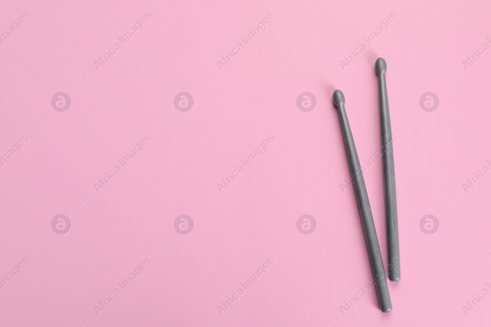 Photo of Two grey drumsticks on pink background, top view. Space for text