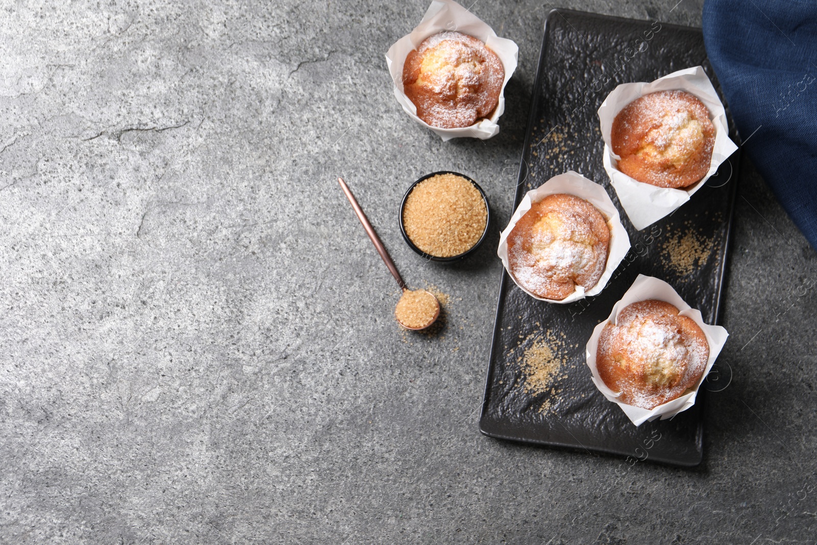 Photo of Delicious muffins and sugar on grey table, flat lay. Space for text