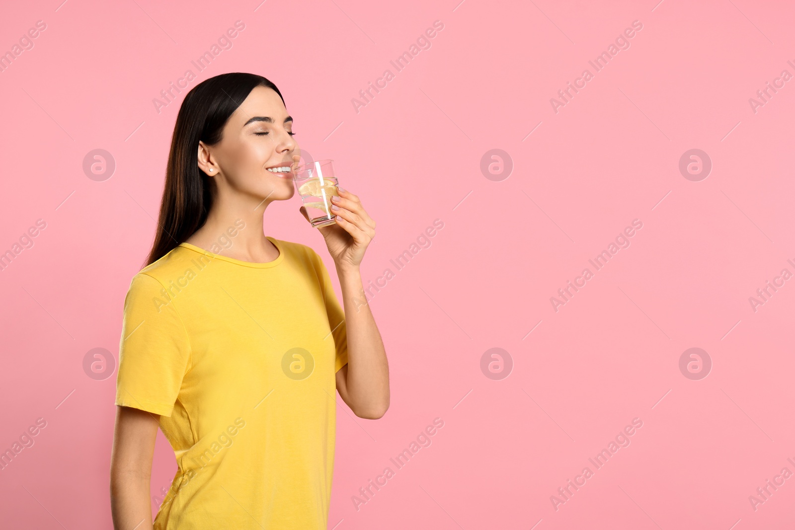 Photo of Beautiful young woman drinking tasty lemon water on pink background. Space for text